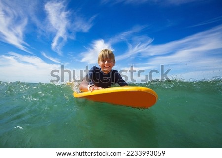 Close face portrait of smiling boy lay on the surf board looking at camera in the sea