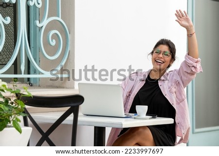 Smiling latin young woman with laptop sitting at sidewalk cafe - stock photo