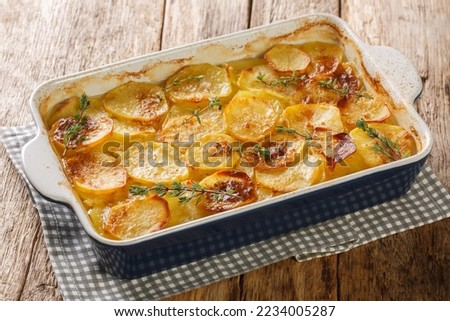 Scalloped potatoes, potato casserole with the addition of herbs, onion and garlic in a ceramic baking dish closeup on the table. Horizontal

