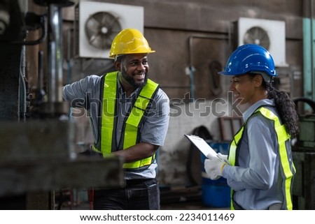 Happy African American male and female engineers in safety vest and helmet working at heavy metal industrial factory. Two technician foreman discussing for checking and repairing machine at factory. Royalty-Free Stock Photo #2234011469