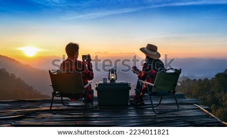 Romantic couple camping outdoors and taking photos with camera while camping at sunrise. Doi Luang Chiang Dao mountains in Chiang Mai.