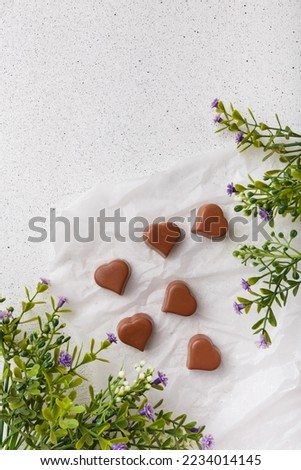 14 February Heart shaped chocolates, green leaves on white paper. Valentines day sweets