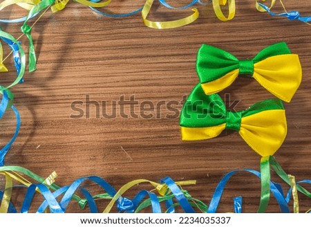Bow tie with brazil colors on a wooden table with green, yellow and blue ribbons.