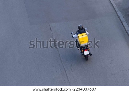 Delivery service from cafes and restaurants, a courier on a scooter with a yellow backpack travels around the city. A courier delivers food on a motorcycle. Fast delivery of food to customers. Royalty-Free Stock Photo #2234037687