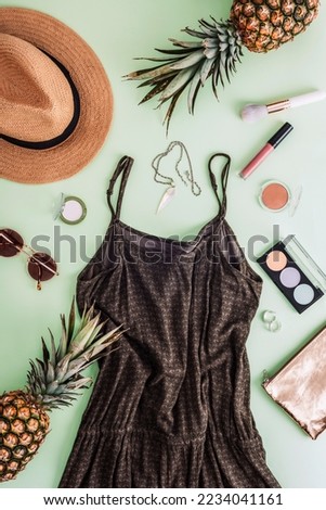 Stylish woman clothes and accessories. Summer dress, sunglasses, straw hat, makeup cosmetics and jewelry on light green background. Flat lay, top view.