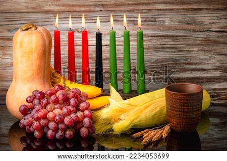 Kwanzaa holiday concept with traditional lit candles, pumpkin, corns, grapes, banana, bowl and of wheat with reflection over black background