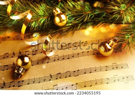 Fir branches, golden streamer and Christmas balls on music sheets, closeup