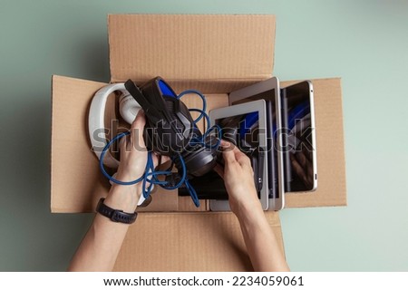 Woman hand collect old used computers, digital tablets, smartphones, electronic devices to cardboard box. Top view. Donation, charity, e-waste, electronic gadgets for reuse, refurbish, recycle concept Royalty-Free Stock Photo #2234059061