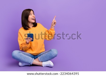 Full body length photo of young excited nice lady sitting finger pointing surprised mockup offer online shopping hold phone isolated on purple color background