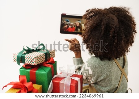 African American young woman in knitted sweater holding tablet while online calling with her family to show gift box nearby, she is happy to get present for Christmas festival and happy new year's.