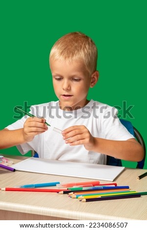 Boy closes lid of green marker. On table there are pencils, brush, book, cubes, paints. Free time, learning to draw, hobbies. Selective focus.