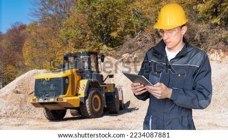 Engineer in a helmet with a digital tablet on the background of construction machine
