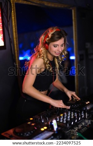 beautiful positive girl DJ blonde energetic plays and listens to music in a nightclub, party, at the remote