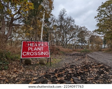 Heavy plant crossing warning sign along a path in the forest.