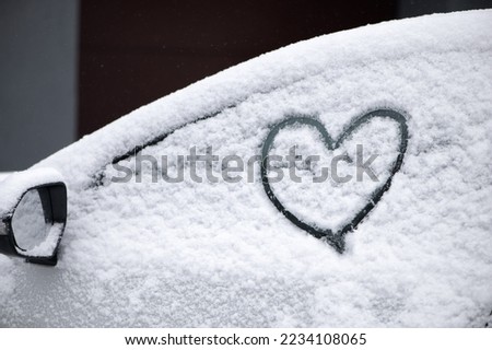 Lovely heart symbol drawn by hand on snowy car window at day light. Christmas and New Year concept