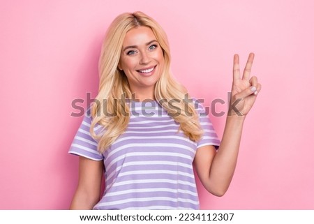 Photo of mature age smiling blonde curly hair woman wear striped purple t-shirt showing v-sign hello everybody isolated on pink color background