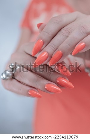 Woman hand with long nails and orange neon manicure holds a bottle of nail polish