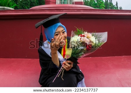 Woman crying tears of joy on her graduation day. Girl holding bouquet of flowers crying on graduation day. Graduation Day at Yogyakarta State University Royalty-Free Stock Photo #2234137737