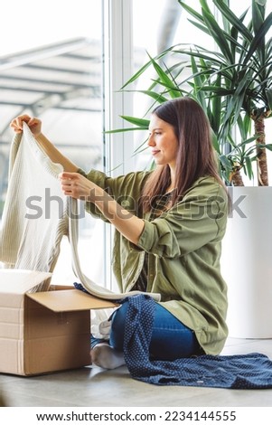 Vertical photo of a woman looking trough the clothes she bought online, taking them out of the box
