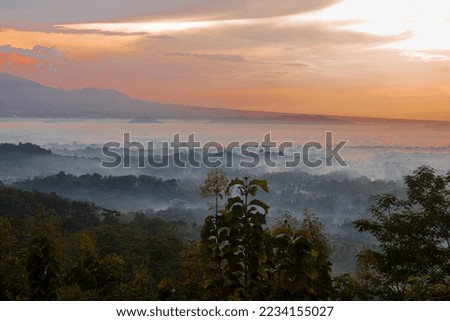 Beautiful panorama of sunrise with layers of orange clouds and fog covering the surrounding area seen from the top of Punthuk Setumbu hill, Indonesia.  Morning vibes