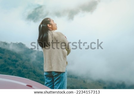 Rear view of a young woman standing on the top of a calm mountain and looking at the morning clouds. Woman wearing a sweater enjoying the beauty of nature looking at the mountain in winter.