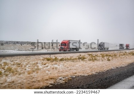 Convoy of industrial big rigs semi trucks with semi trailers transporting commercial cargo moving cautiously on a slippery highway during a winter snow storm in Shasta Lake area in California Royalty-Free Stock Photo #2234159467