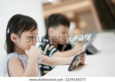 Little asian boy and girl enjoying modern generation technologies playing indoors using tablet pc. Soft focus. Copy space.