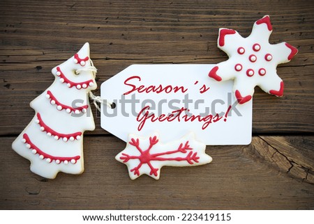 Red Season's Greetings on a white Label with white and red Decorated Christmas Cookies, on Wood