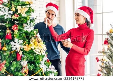 Romantic sweet couple in santa hats having fun decorating christmas tree and smiling while celebrating new year eve and enjoying spending time together in christmas time at home