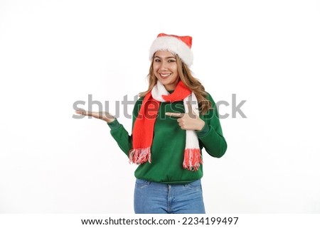 Attractive excited asian female in green sweater with santa hat on christmas isolated on white background. Pointing