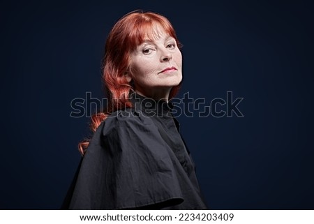Senior people. Fashion and beauty. Portrait of a good-looking elderly woman with bright red hair dressed in a black blouse. Studio portrait on a dark blue background with copy space.