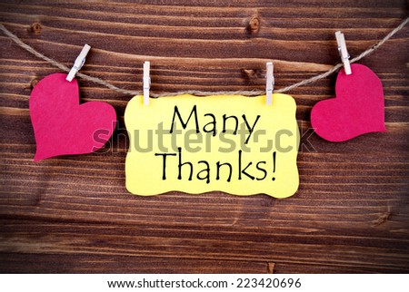 The Words Many Thanks standing on a Yellow Label, framed by two red Hearts hanging on a Line on wooden Background