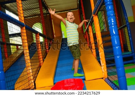 Cheerful little boy playing in the children's entertainment center.Cute child boy near a roller coaster with a plastic red sledge on the playground in the children's play center	 Royalty-Free Stock Photo #2234217629