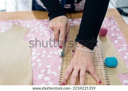 Unrecognized woman working in bright fashion workshop. She is cutting the fabrics.