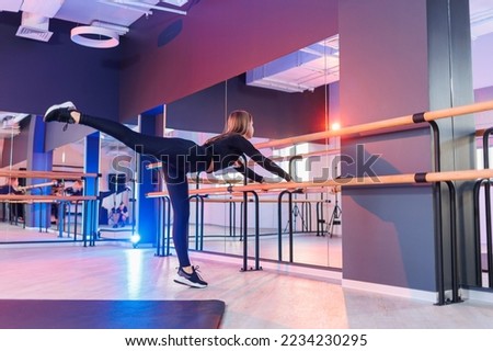 Young beautiful flexible woman in a black suit sits on the floor and works hard on herself and stretches