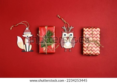 Christmas gift boxes with funny cute decorations on a red background. Set of wooden fox and owl toys.