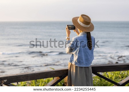 Travel woman use cellphone to take photo at seaside under sunset period