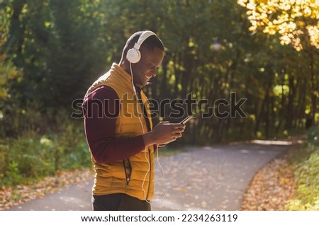 Portrait African american man listens music in autumn park copy space and place for advertising. Gadget, app and streaming service concept