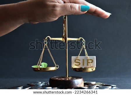 Savings and investment concept with hand placed above weighing scale with SIP written on block and new leaves in comparison. Royalty-Free Stock Photo #2234266341