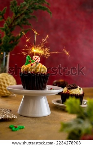 Christmas Cupcake with sparkler on cake stand, colorful burguny background. Moody lifestyle imag