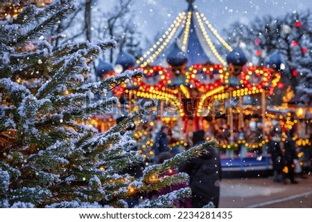 Christmas in Tivoli Gardens, Copenhagen, Denmark, with a snow covered fir tree in front of a defocussed carrousel ride