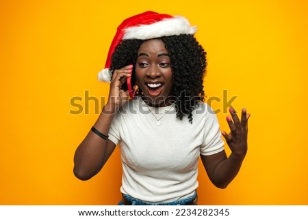 African young woman with santa claus hat talking on mobile phone against yellow background.