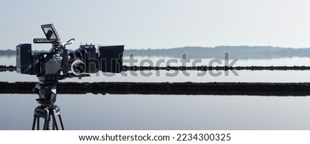 Professional video camera with lake landscape background. Documentary film or movie production banner with copy space. Royalty-Free Stock Photo #2234300325