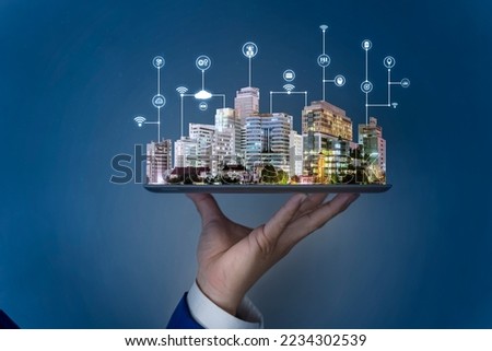 Businessman hand holding tablet then land, trees and tall buildings on it, selling real estate online. Devices connected to digital storage in data center via internet. IOT. Smart home.