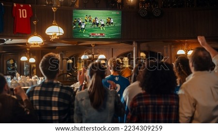 Group of American Football Fans Watching a Live Match Broadcast in a Sports Pub on TV. People Cheering, Supporting Their Team. Crowd Goes Ecstatic When Team Scores a Goal and Wins the Championship. Royalty-Free Stock Photo #2234309259