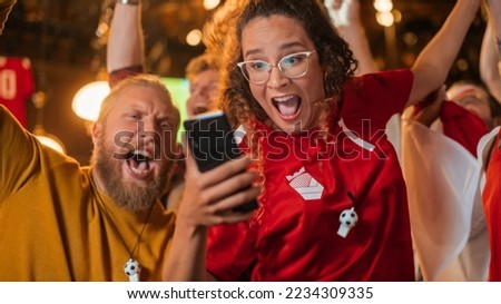 Excited Female Holding a Smartphone, Nervous About the Sports Bet She Put on a Her Favorite Soccer Team. Ecstatic Emotions When Football Team Scores a Goal and She Wins a High Stakes Lottery Prize. Royalty-Free Stock Photo #2234309335