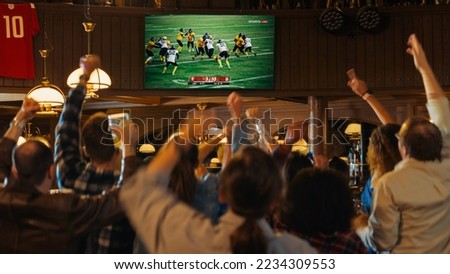 Group of American Football Fans Watching a Live Match Broadcast in a Sports Pub on TV. People Cheering, Supporting Their Team. Crowd Goes Ecstatic When Team Scores a Goal and Wins the Championship. Royalty-Free Stock Photo #2234309553