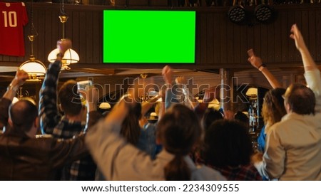 Group of Multicultural Friends Watching a Live Sports Match on TV with Green Screen Display in a Bar. Happy Fans Cheering and Shouting, Celebrating When Team Scores a Goal and Wins the Tournament. Royalty-Free Stock Photo #2234309555