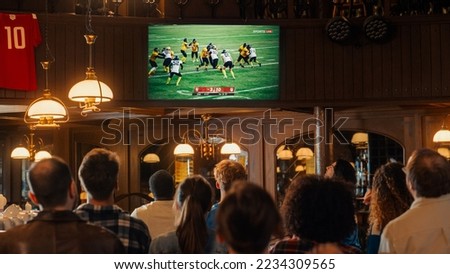 Group of American Football Fans Watching a Live Match Broadcast in a Sports Pub on TV. People Cheering, Supporting Their Team. Crowd Goes Ecstatic When Team Scores a Goal and Wins the Championship. Royalty-Free Stock Photo #2234309565