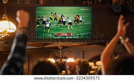 Group of American Football Fans Watching a Live Match Broadcast in a Sports Pub on TV. People Cheering, Supporting Their Team. Crowd Goes Ecstatic When Team Scores a Goal and Wins the Championship. Royalty-Free Stock Photo #2234309571